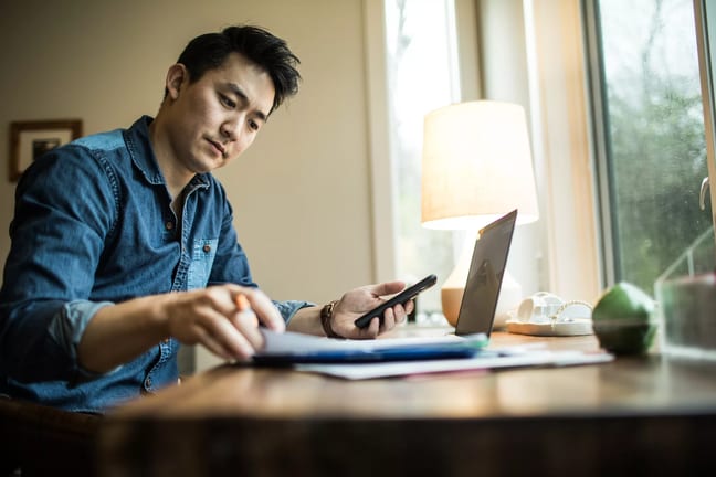 person in home office holding smartphone and looking at document.jpg