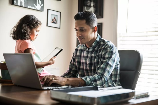 person sitting at a desk looking at a laptop with a child nearby.jpg