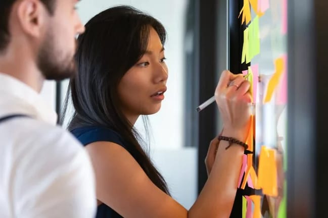 woman in office writing on post its next to m.width VHmiFiK.jpg