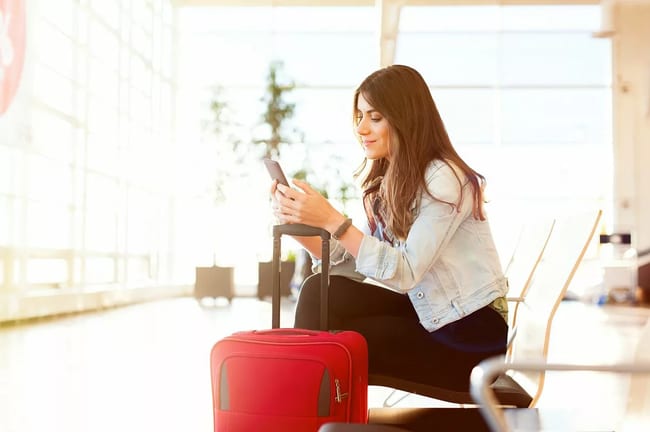 smiling woman with suitcase on phone in airpo.width KCyX.jpg