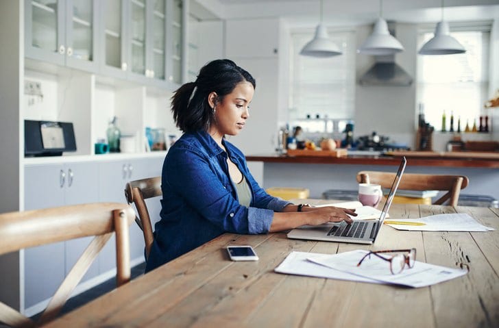 woman at kitchen table with laptop and paperw.width nlFF