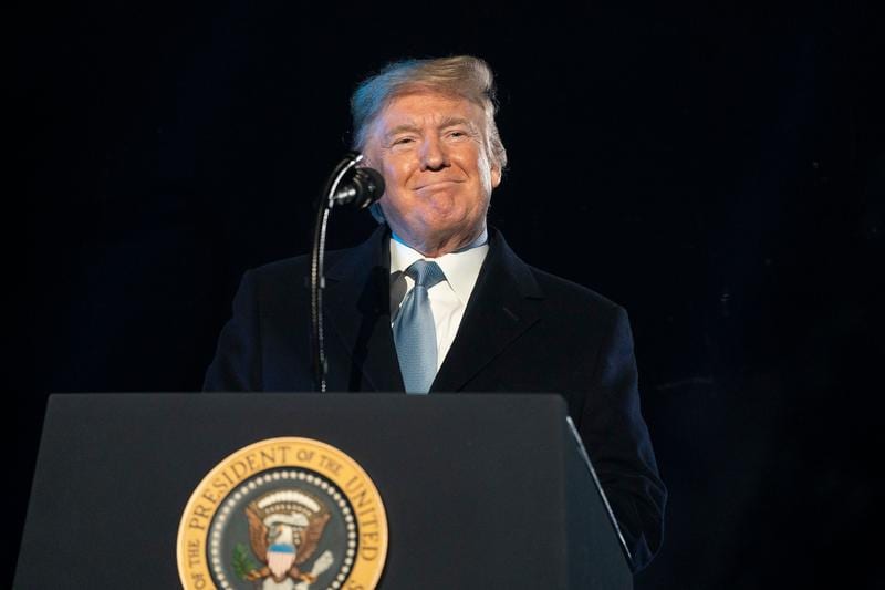 Donald Trump is smiling while standing behind the presidential podium.