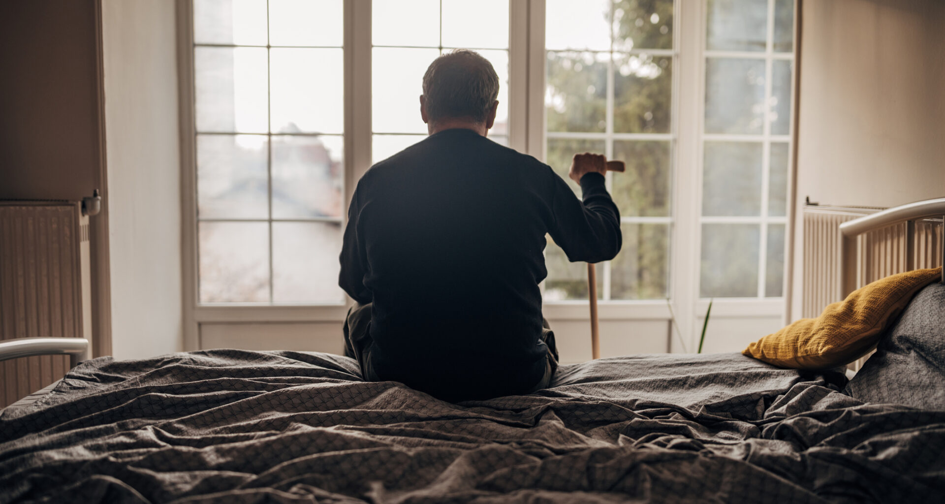 retired man with cane sitting on bed