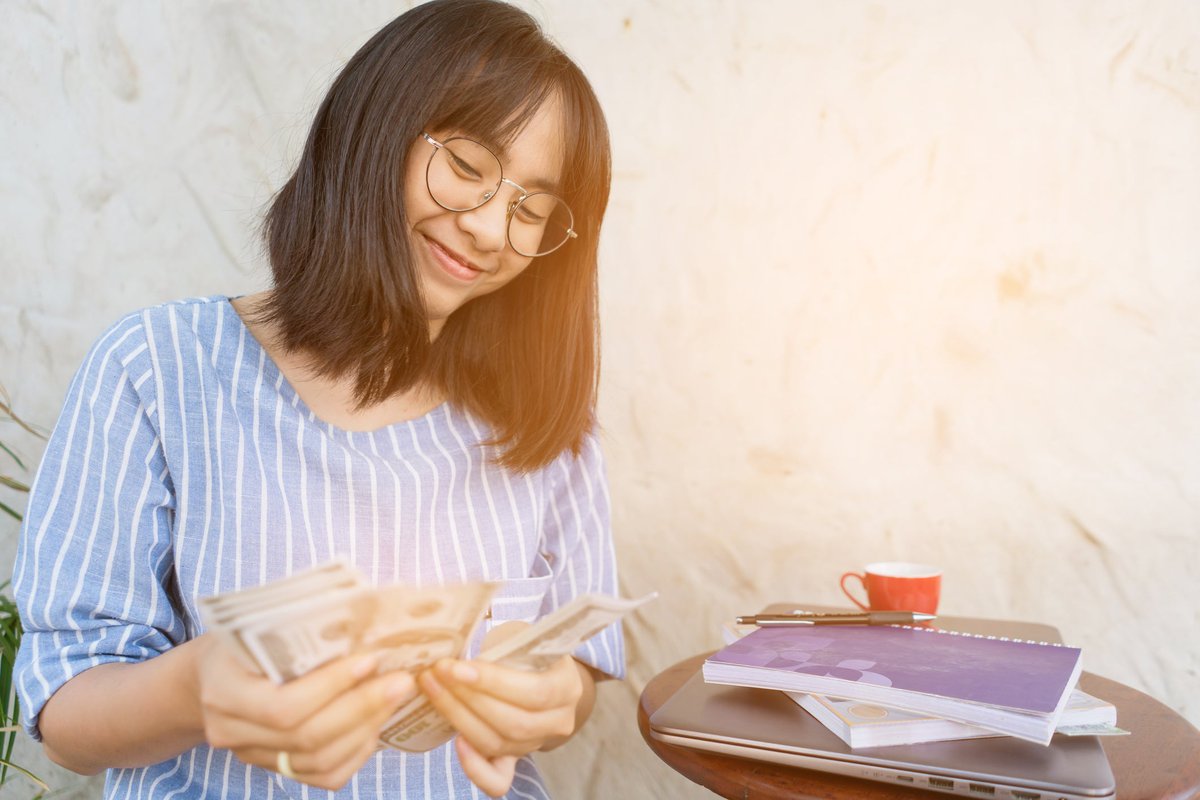 Young woman smiling as she counts cash in her.width XDyly.jpg